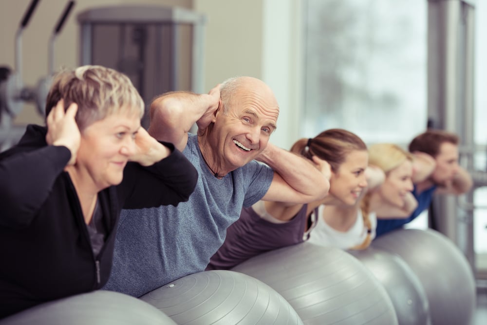 Elderly couple doing pilates class at the gym with a group of diverse younger people balancing on the gym ball with raised arms to tone their muscles in an active retirement concept Elderly couple doing pilates class at the gym with a group of diverse younger people balancing on the gym ball with raised arms to tone their muscles in an active retirement concept